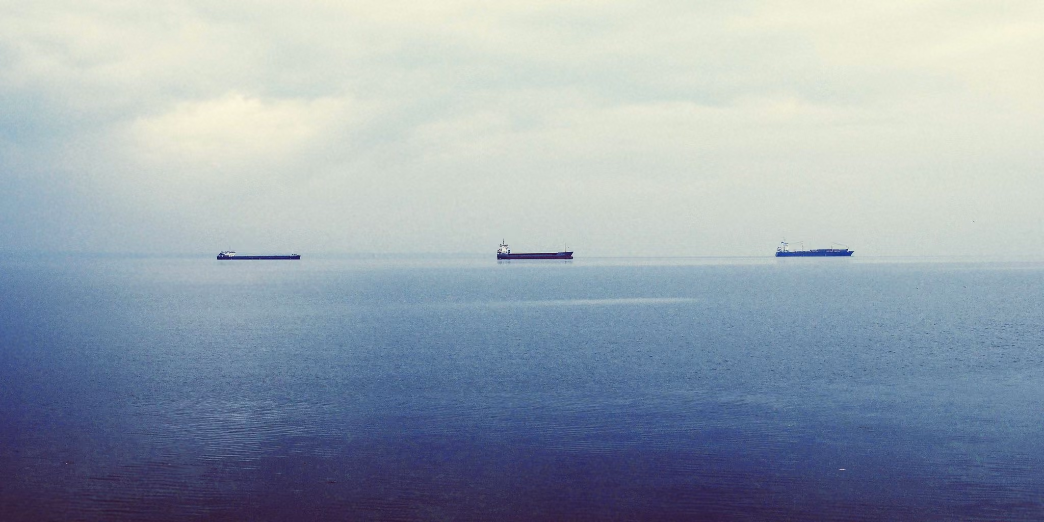 Três navios de carga na linha do horizonte, num mar calmo